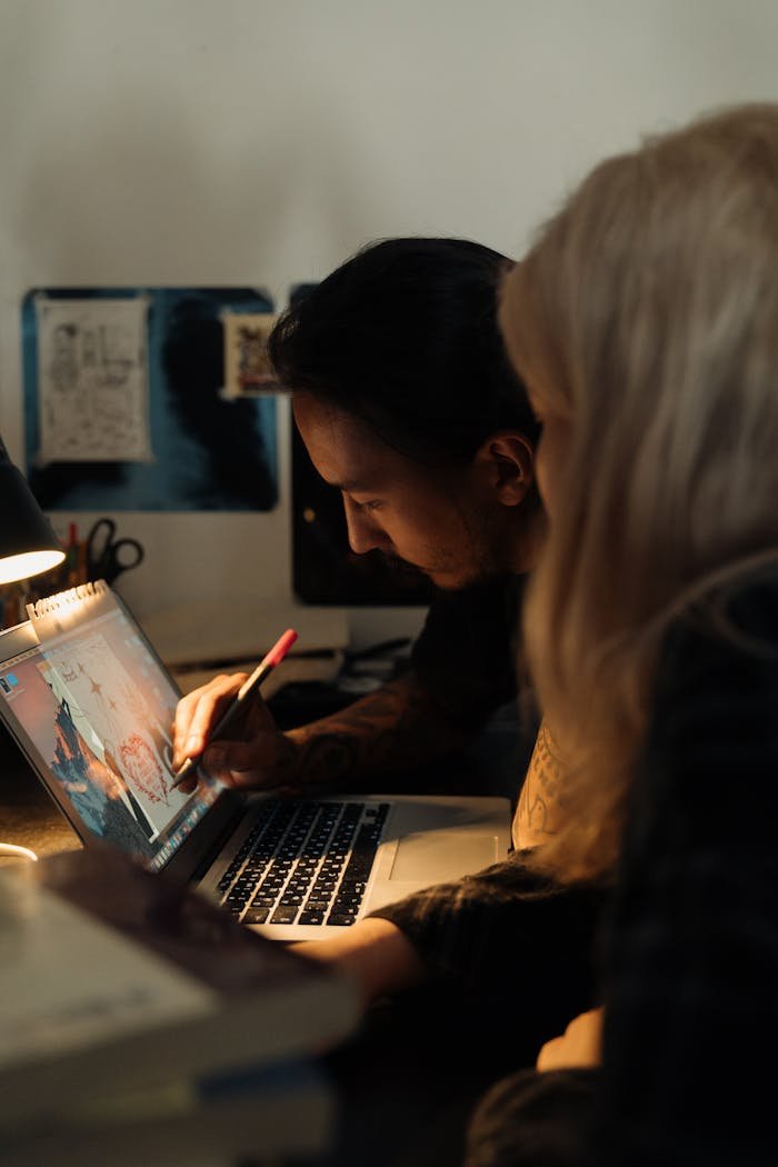 Two adults working on a creative project using a laptop at a desk indoors.